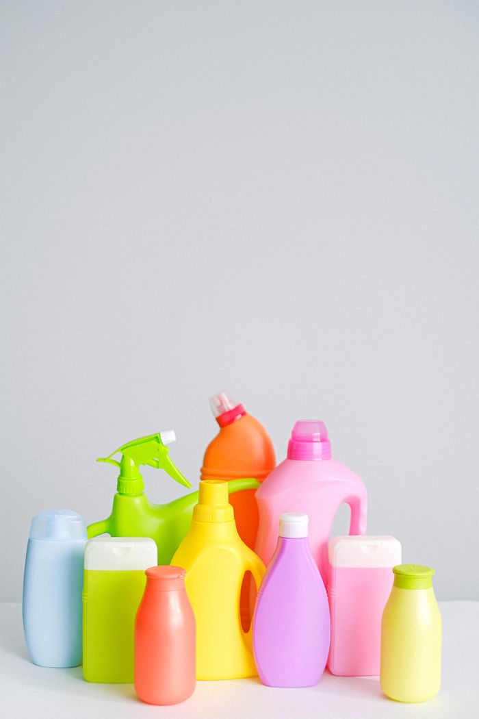 Set of various multicolored plastic bottles with detergents for household routine placed on table against white background in light studio